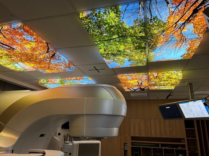 Radiation therapy linear accelerator with illuminated nature ceiling panels displaying autumn foliage and blue sky